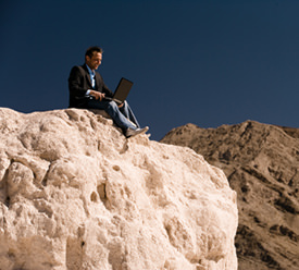 Man continueing his online Christian college education while sitting on a rock.